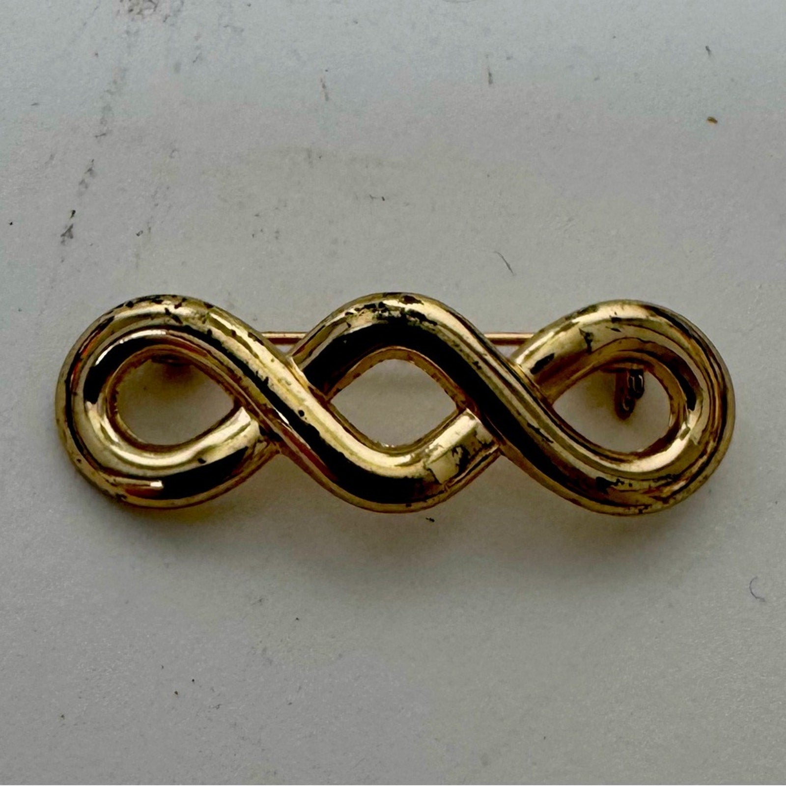 Gold Infinity pin with a closure that rotates around to keep it secure